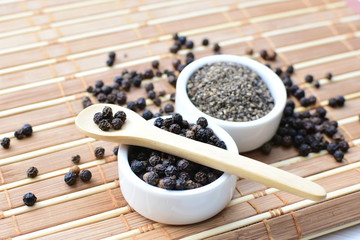Whole and ground black peppercorns on white wooden background