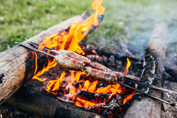 Rustic sausage on a skewer at the stake - sausages are fried over an open fire in the forest - camping food