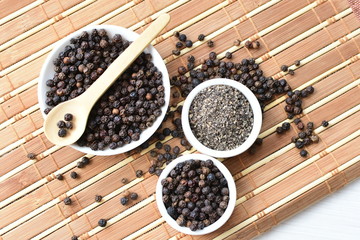 Whole and ground black peppercorns on white wooden background