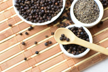 Whole and ground black peppercorns on white wooden background