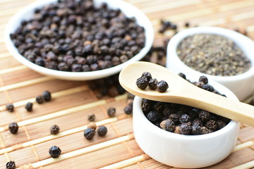 Whole and ground black peppercorns on white wooden background
