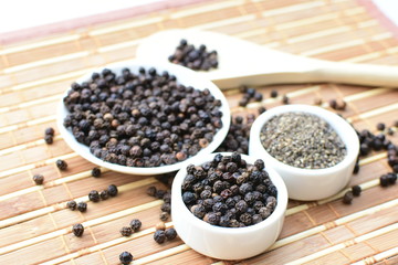 Whole and ground black peppercorns on white wooden background
