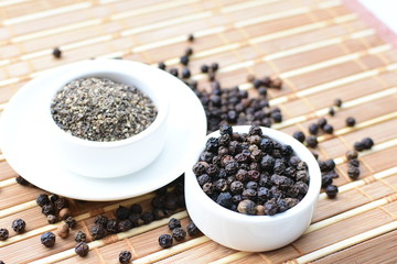 Whole and ground black peppercorns on white wooden background