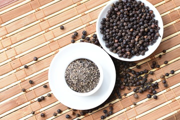 Whole and ground black peppercorns on white wooden background