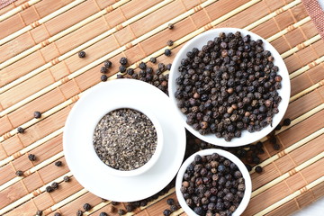 Whole and ground black peppercorns on white wooden background