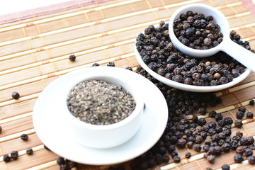 Whole and ground black peppercorns on white wooden background