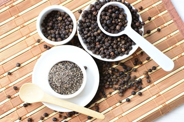 Whole and ground black peppercorns on white wooden background