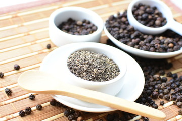 Whole and ground black peppercorns on white wooden background
