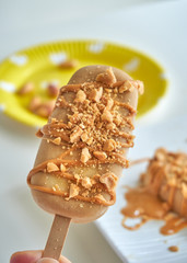 Hand holding peanut butter banana popsicles with sprinkles of peanuts and drizzle of raw peanut...