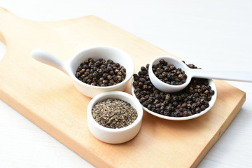 Whole and ground black peppercorns on white wooden background