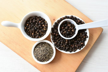 Whole and ground black peppercorns on white wooden background