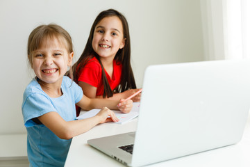 Cool online school. Kids studying online at home using a laptop. Cheerful young little girls using...