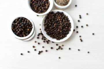 Whole and ground black peppercorns on white wooden background