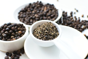 Whole and ground black peppercorns on white wooden background