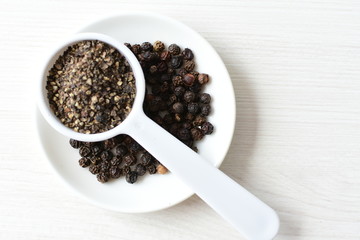 Whole and ground black peppercorns on white wooden background