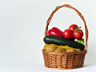 Wicker basket full of vegetables, zucchini, eggplant, tomatoes, peppers, potatoes. On a white background.