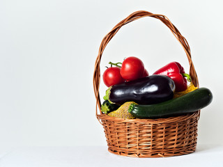 Wicker basket full of vegetables, zucchini, eggplant, tomatoes, peppers, potatoes. On a white background.