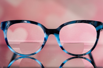 Eyeglasses Glasses with Bifocals and Black and blue Frame smudged view agaist a blurry pink  background with white hearts. Blurry Vision Concept