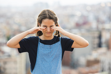 Little girl rubbing her eyes for itchiness in the city