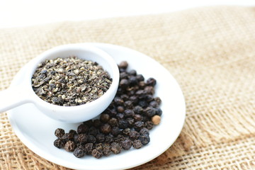 Whole and ground black peppercorns on white wooden background