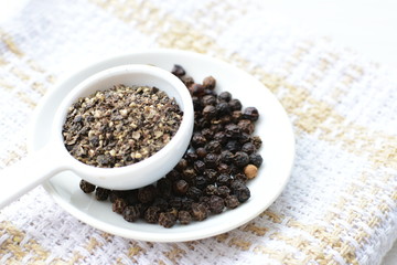 Whole and ground black peppercorns on white wooden background
