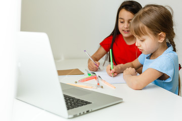 Two girls, the oldest and the youngest, are engaged at a table on a laptop.