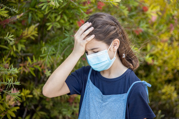 Little girl with protective mask suffering headache in the park