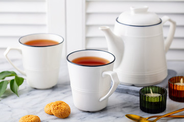 Tea in mugs with teapot on marble background. Close up.