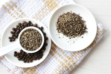 Whole and ground black peppercorns on white wooden background