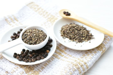 Whole and ground black peppercorns on white wooden background