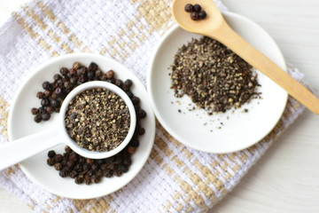 Whole and ground black peppercorns on white wooden background
