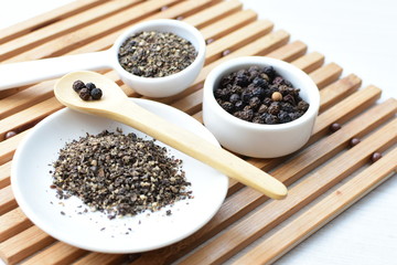 Whole and ground black peppercorns on white wooden background