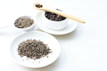 Whole and ground black peppercorns on white wooden background