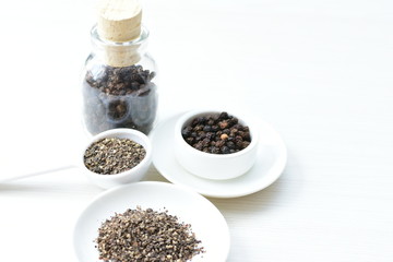 Whole and ground black peppercorns on white wooden background