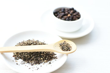 Whole and ground black peppercorns on white wooden background