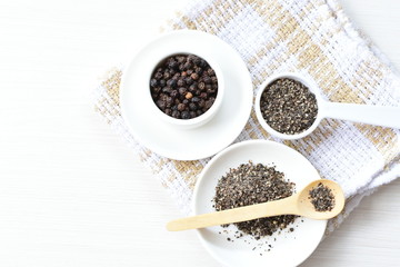 Whole and ground black peppercorns on white wooden background