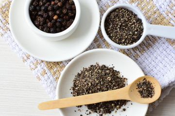 Whole and ground black peppercorns on white wooden background