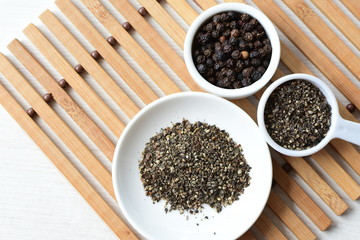 Whole and ground black peppercorns on white wooden background