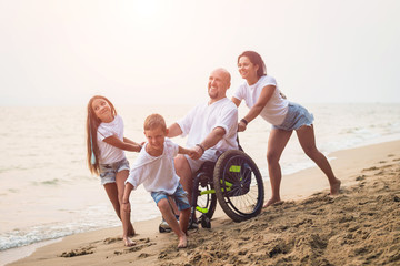 Disabled man in a wheelchair with his family on the beach.