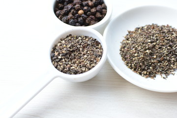 Whole and ground black peppercorns on white wooden background