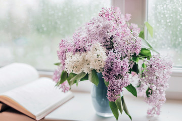 Bouquet of lilacs in a vase,cup of coffee and books on the windowsill