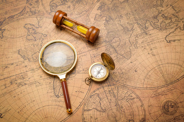 Obraz na płótnie Canvas Old compass , magnifying glass and sand clock on vintage map