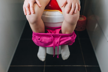 Little girl is sitting on the toilet in the bathroom. Photography, concept.