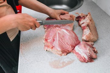 A girl, a hostess, a butcher cuts with a knife raw, fresh, bloodied pork meat for cooking in the...
