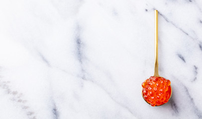 Red salmon caviar in golden spoon. Marble background. Copy space. Top view.