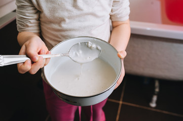 Little girl child holds in his hands a bowl with a spoon, dough, porridge. Photography, concept.