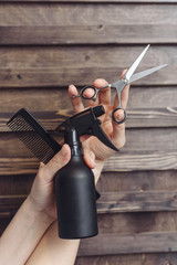 Hairdresser tools on a wooden background in the hands of a master. Dark tint. Protective spray,...