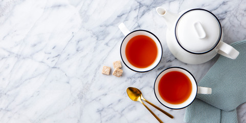 Tea in mugs with teapot on marble background. Copy space. Top view.