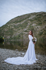 Fototapeta na wymiar A bride in a long wedding dress standing on the shore of a lake