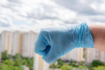 A male hand in a medical glove clenched into a fist against a cityscape